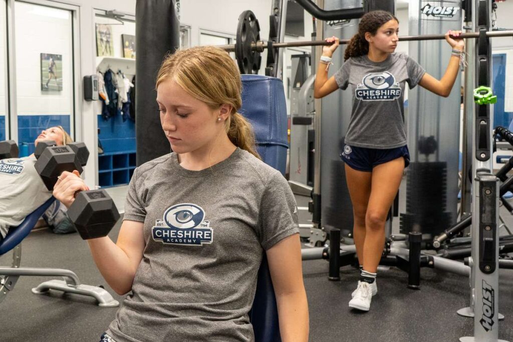 A female Cheshire Academy athlete lifting weights in the Strength and Conditioning center.